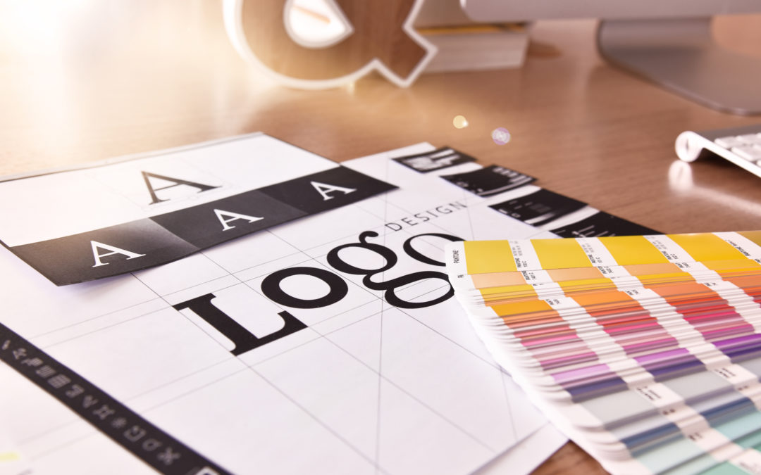 Photo of a graphic designer's desk with the word "Logo" being designed, letter A's in various fonts, and color swatches in the lower right corner.